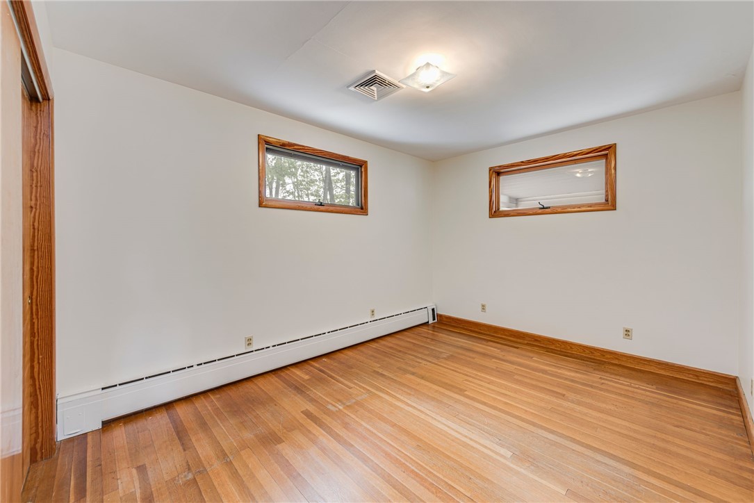 Empty room with polished hardwood floors, two high windows, and a long baseboard heater.