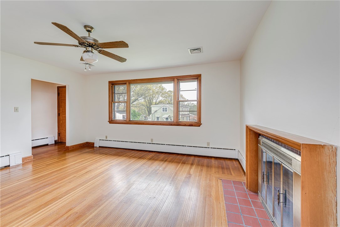 Empty living room with hardwood floors, a wood-trimmed window, and a fireplace.