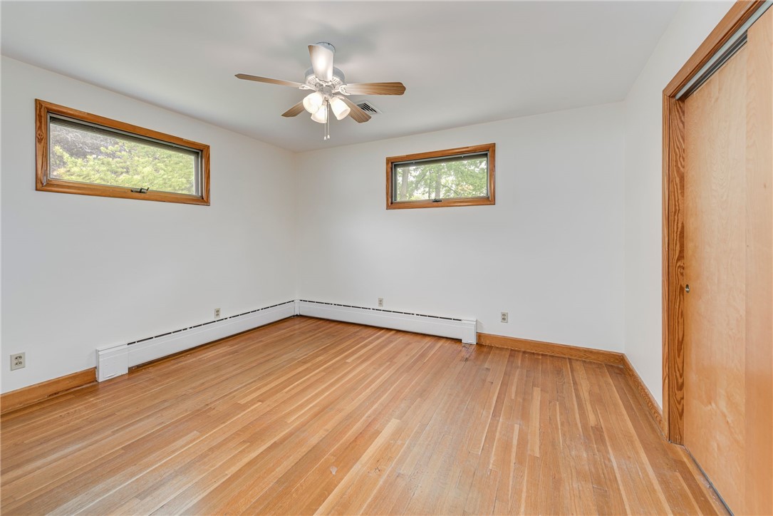Empty bedroom with hardwood floors, two high windows, a ceiling fan, and a sliding wood closet door.