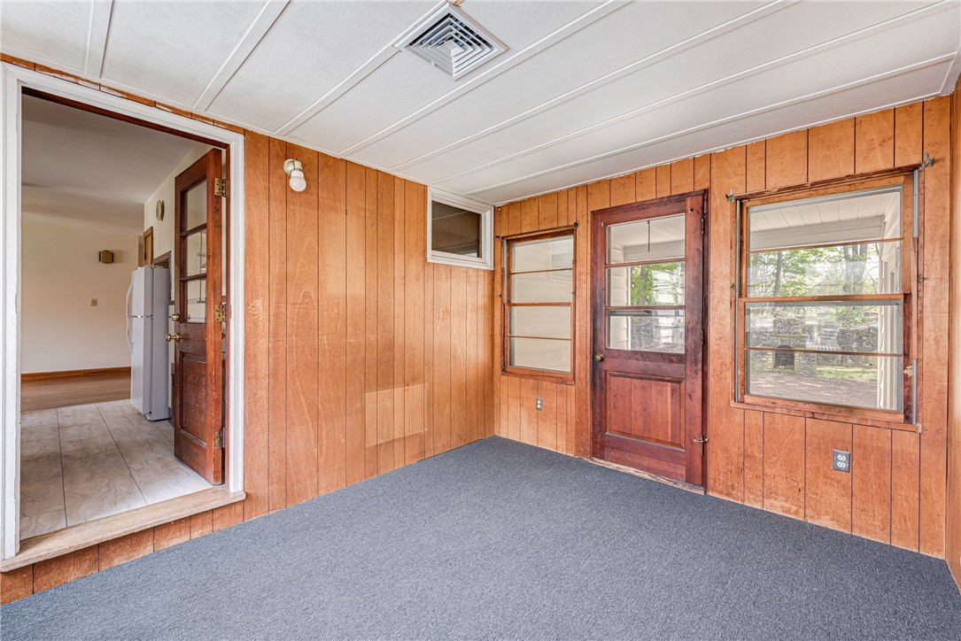 Empty carpeted room with wood-paneled walls and a wooden door flanked by windows.