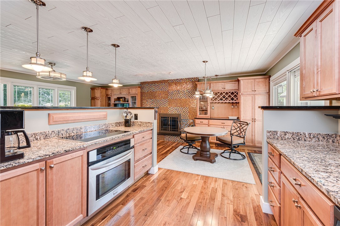 Kitchen with granite counters, wood cabinetry, and a dining nook beside a tiled fireplace.
