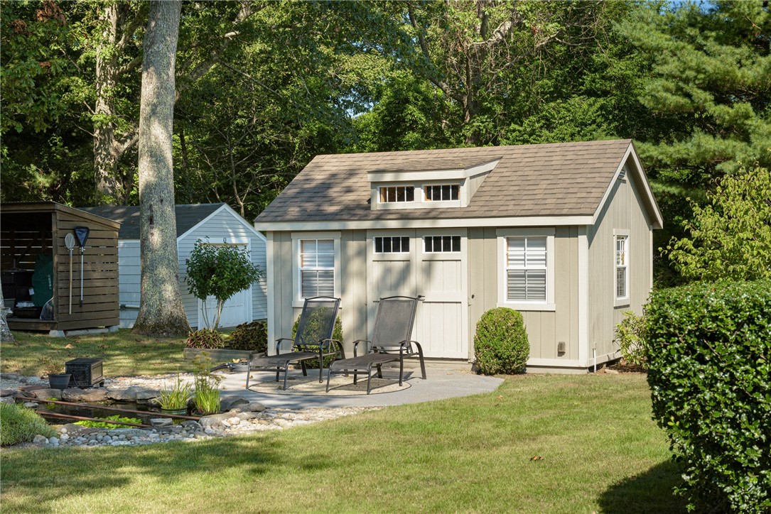 Garden shed with double doors beside a patio, lounge chairs, and a landscaped pond.