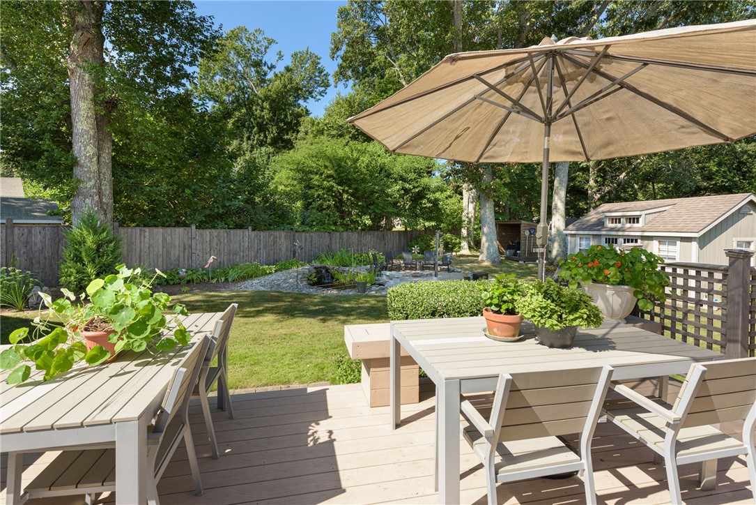 Wooden deck with dining tables and umbrella overlooking a landscaped backyard.