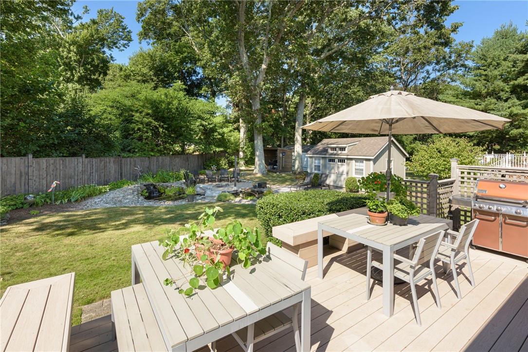 Backyard deck with dining set, umbrella, grill, and landscaped pond beside a small shed.