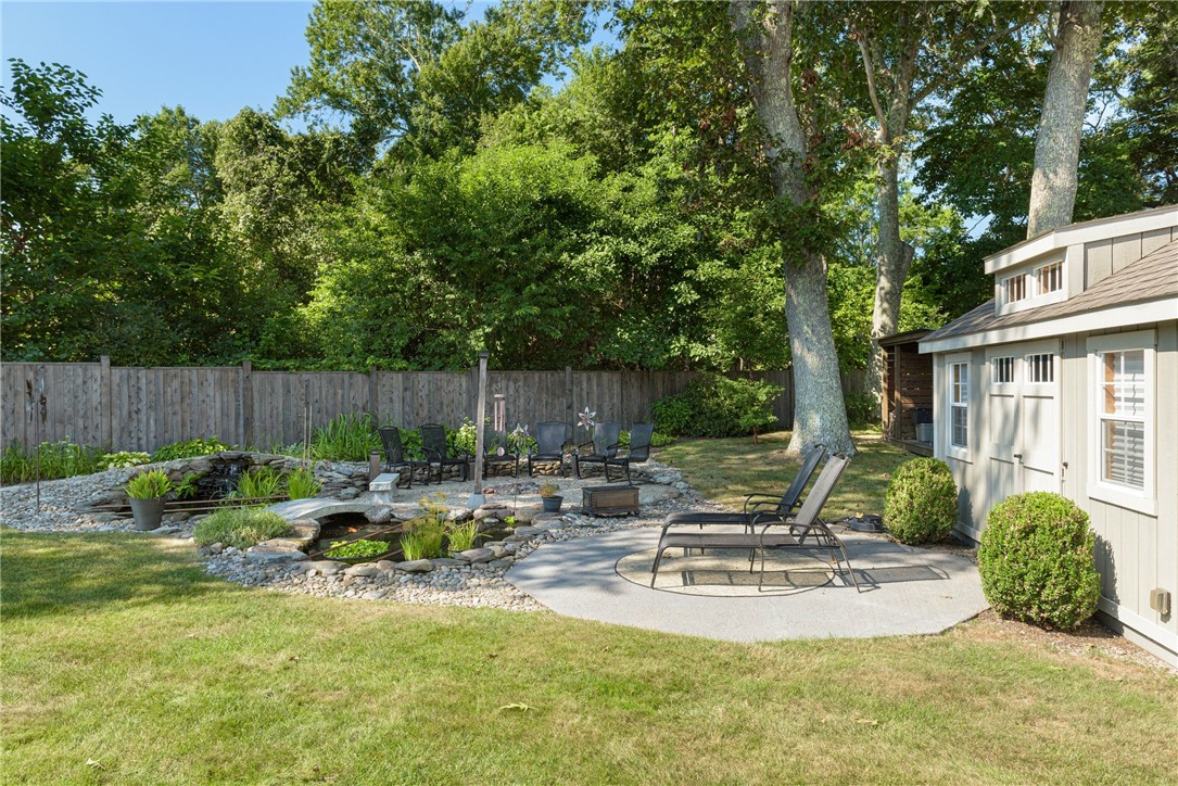 Backyard patio with lounge chairs beside a stone-lined pond and fenced lawn.
