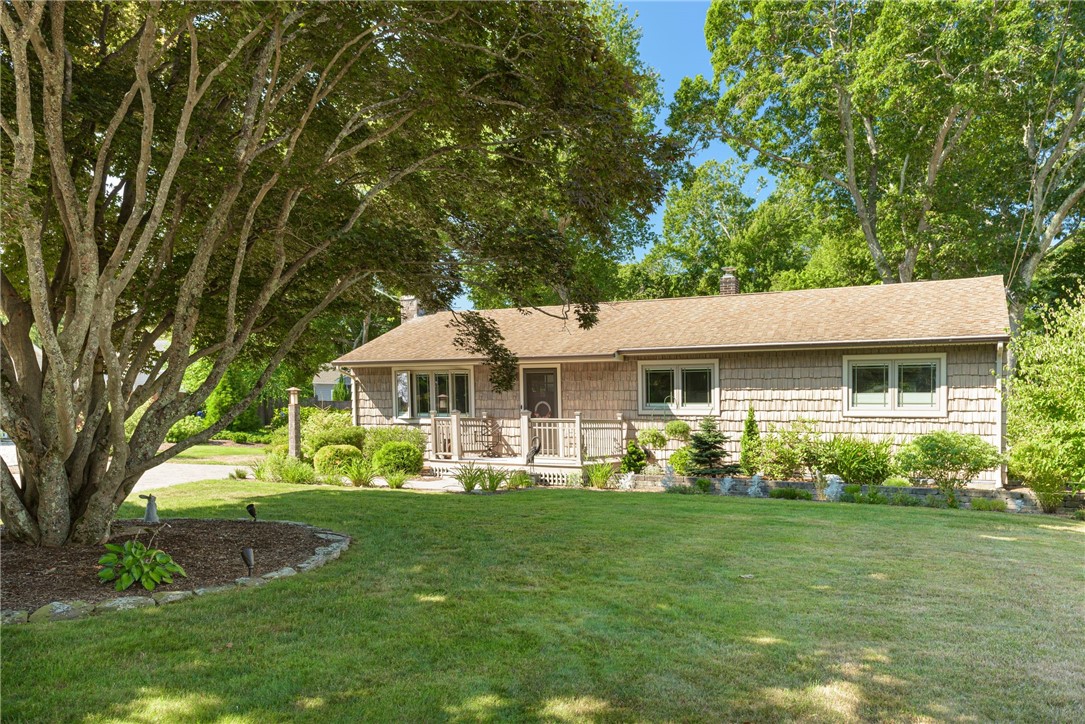 Cedar-shingle home with a small front deck, landscaped lawn, and mature shade trees.