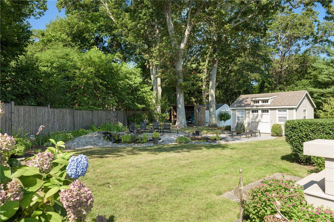 Landscaped backyard with a stone pond, outdoor seating, flowering hydrangeas, and a detached white shed.