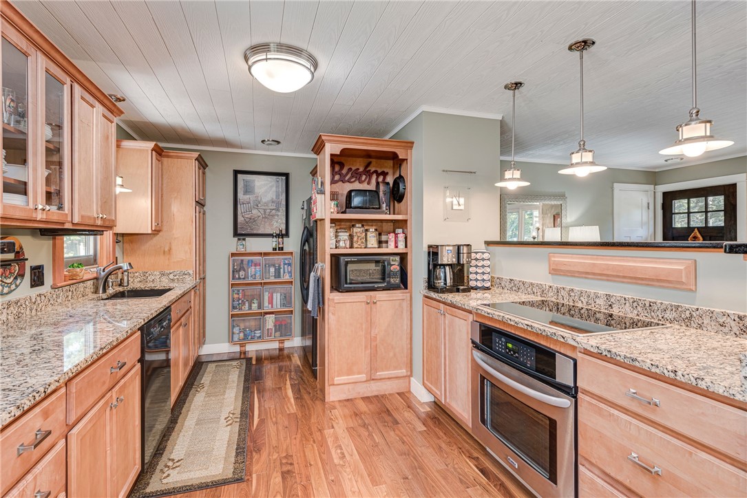 Kitchen with warm wood cabinetry, granite counters, stainless steel appliances, and a central pantry cabinet.