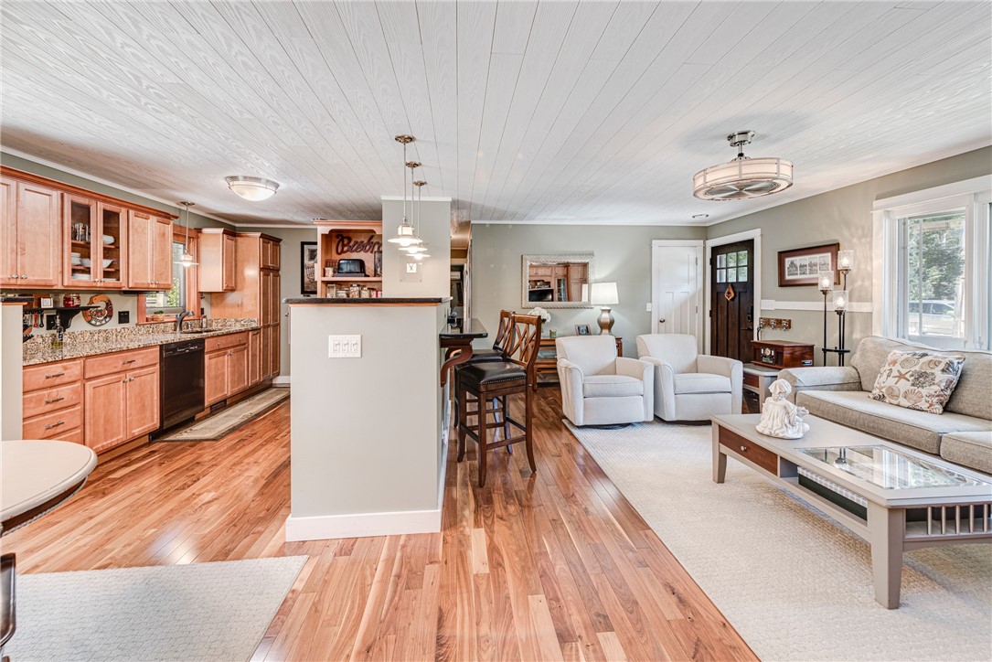 Open-plan kitchen and living room with wood cabinetry, hardwood floors, and a breakfast bar.
