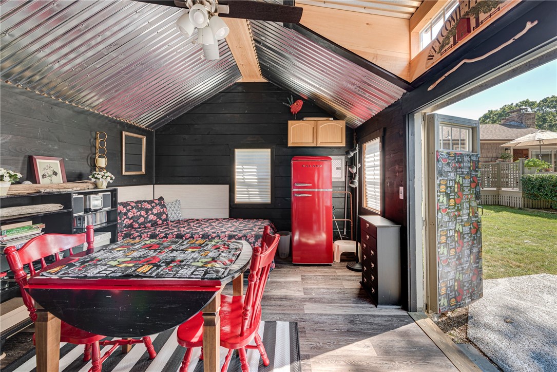 Furnished bonus room with vaulted metal ceiling, red refrigerator, floral sofa, and open doorway to the yard.