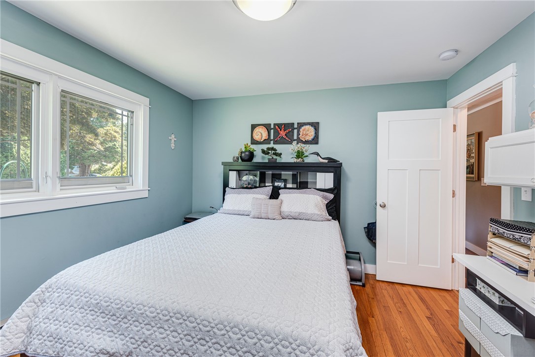 Bedroom with a white quilted bed, pale blue walls, and large windows overlooking trees.