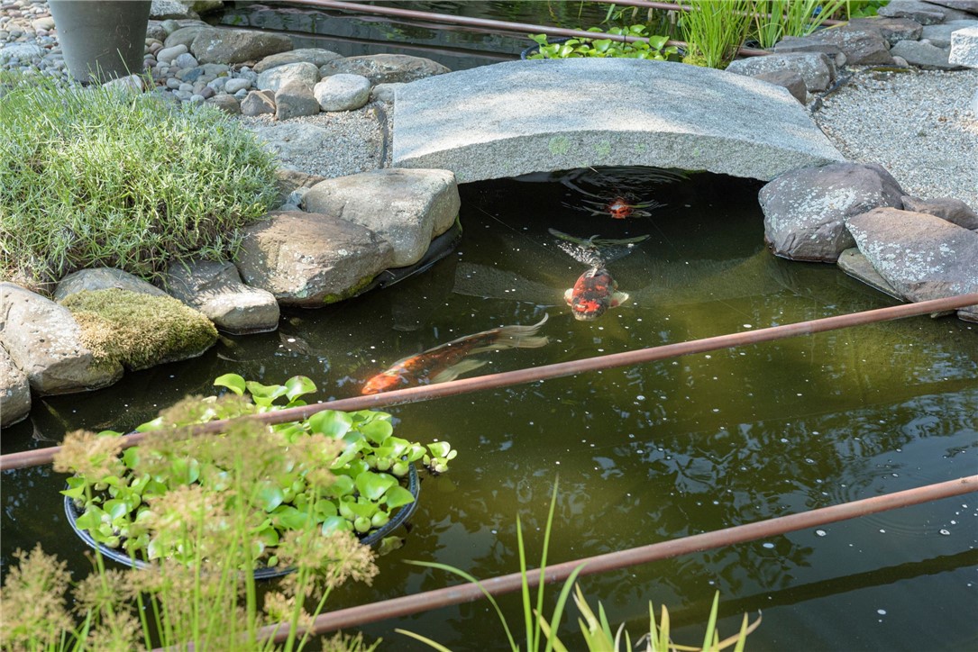 Koi swim in a rock-lined garden pond beneath a flat stone bridge.