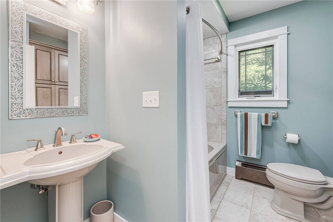 Bathroom with a pedestal sink, tiled shower, and window above a striped towel.
