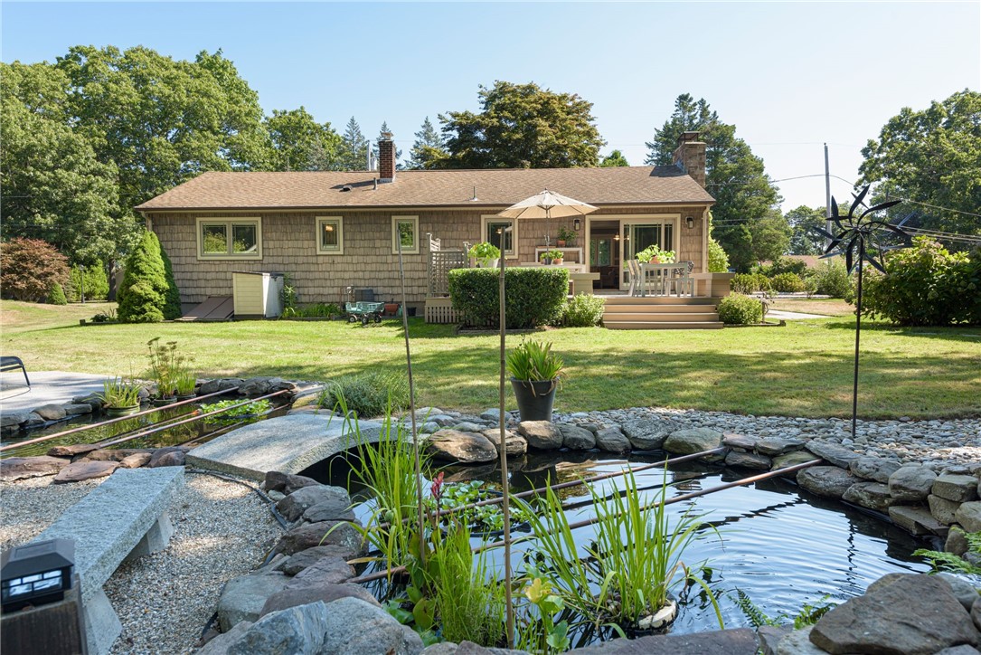 Shingle-sided home with a raised deck behind a landscaped rock-edged pond.