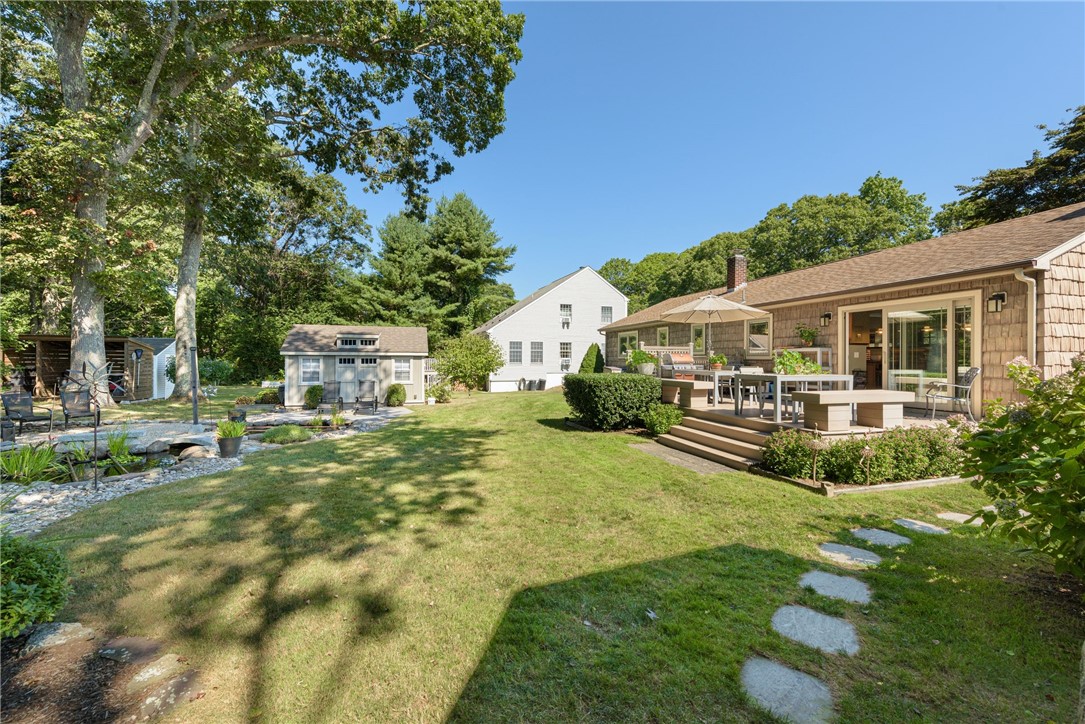 Landscaped backyard with a broad lawn, raised deck, outdoor dining area, and stone garden pond.
