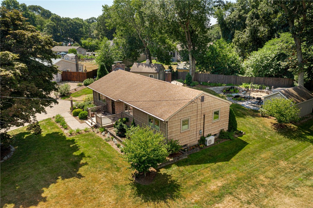 Aerial view of a shingle-sided home with a deck, fenced patio, and mature trees.