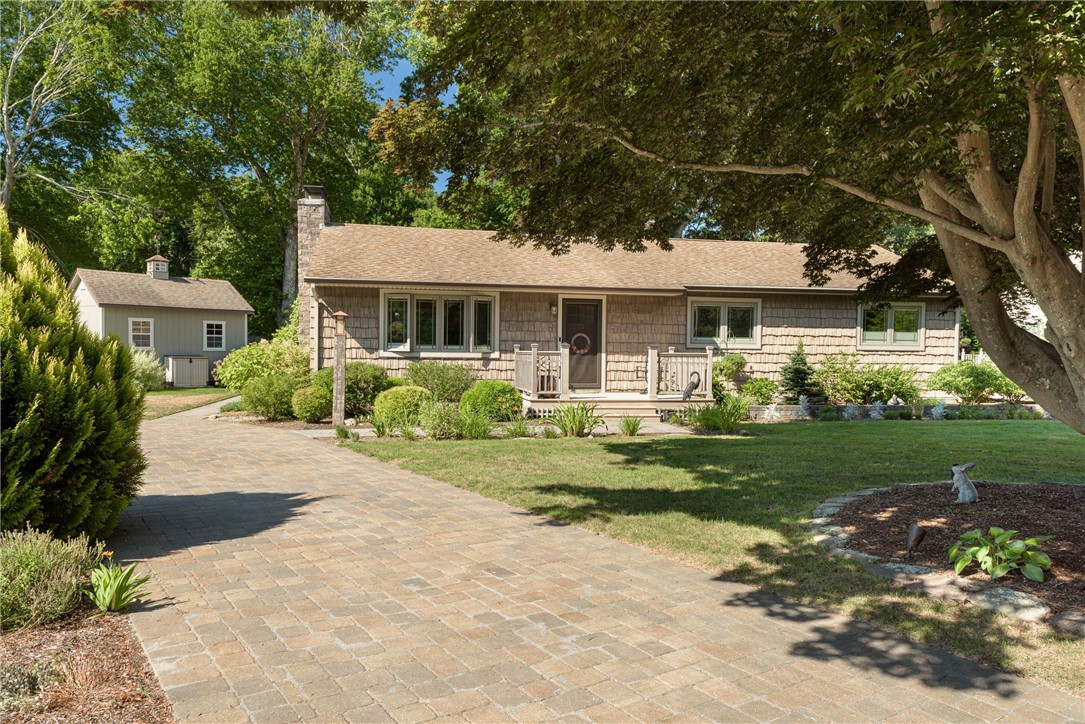 Shingle-sided home with a stone chimney, paved driveway, landscaped lawn, and detached shed.