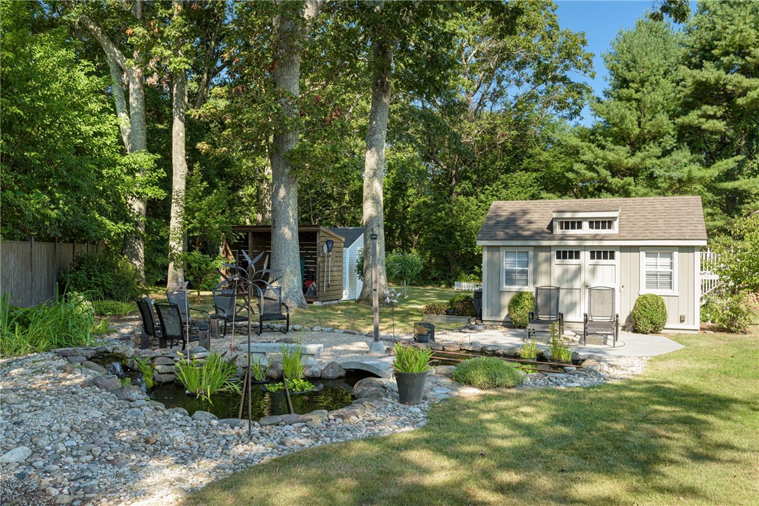 Landscaped backyard with a small pond, patio seating, and a detached shed beneath mature trees.