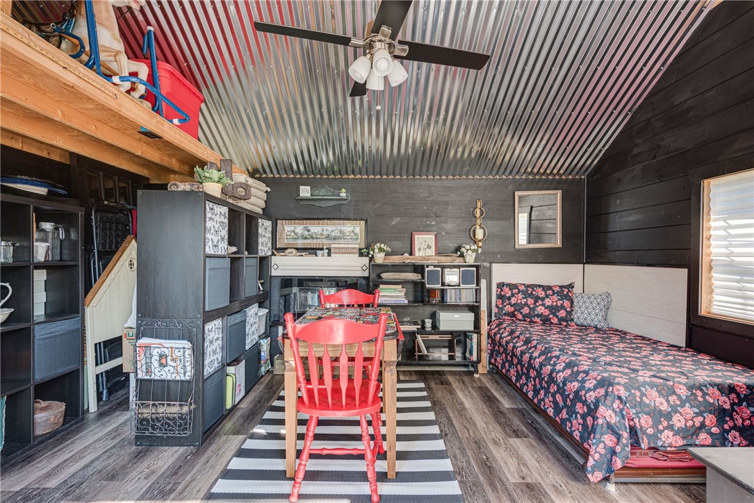 Bedroom with a floral-covered bed, red desk chair, extensive shelving, and corrugated metal ceiling.