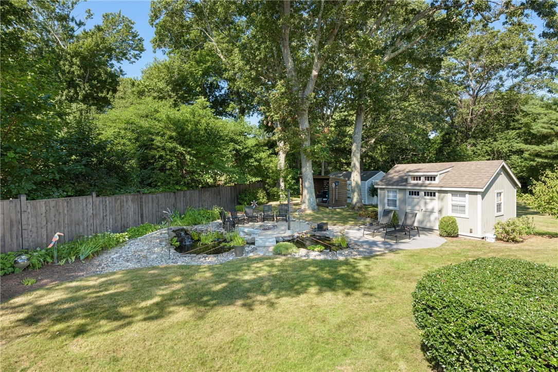 Backyard with a stone-edged pond, patio seating, and a detached gray shed beneath mature trees.