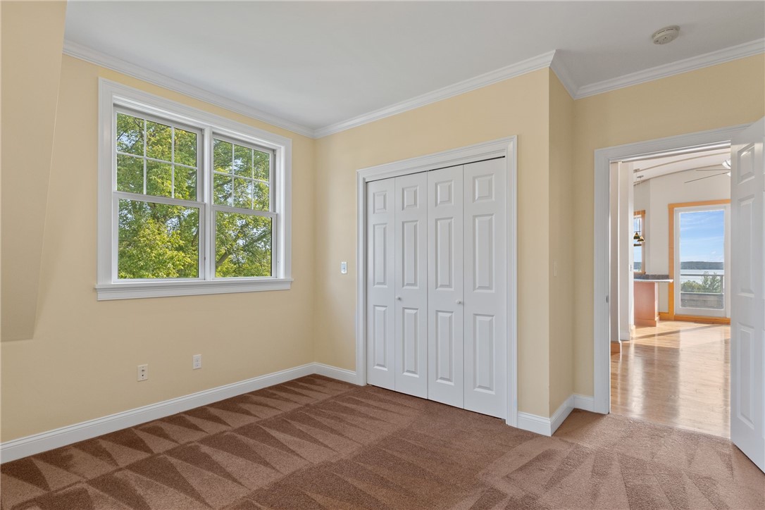 Vacant bedroom with patterned brown carpet, white closet doors, and a window overlooking leafy trees.