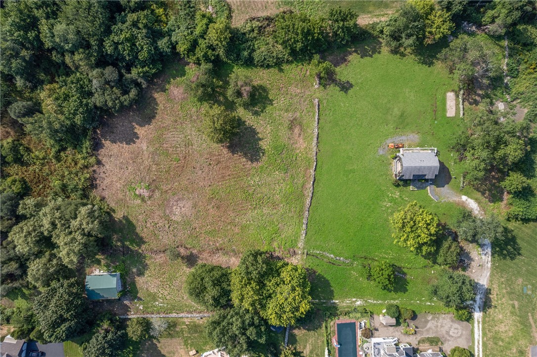 Aerial view of a grassy property bordered by trees, with a small building and stone boundaries.