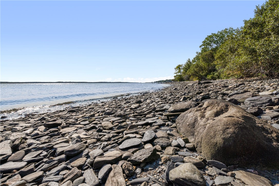 Rocky shoreline beside calm water, with a wooded coast in the distance.