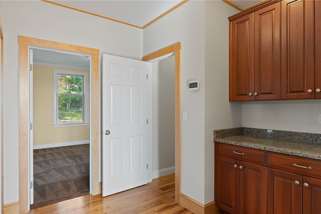 Kitchen with cherry-toned cabinets and stone countertop beside an open doorway to a carpeted room.