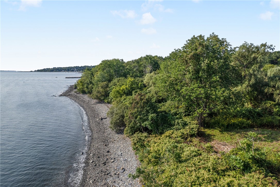 Wooded waterfront shoreline with a rocky beach curving beside calm water.