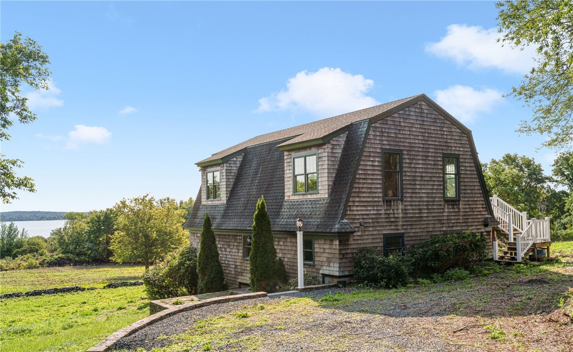 Cedar-shingle home with a gambrel roof and side deck, with water visible beyond the lawn.