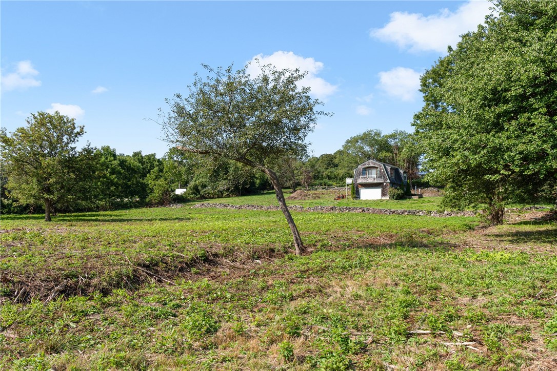 Grassy property lot with scattered trees, a stone wall, and a small house in the distance.