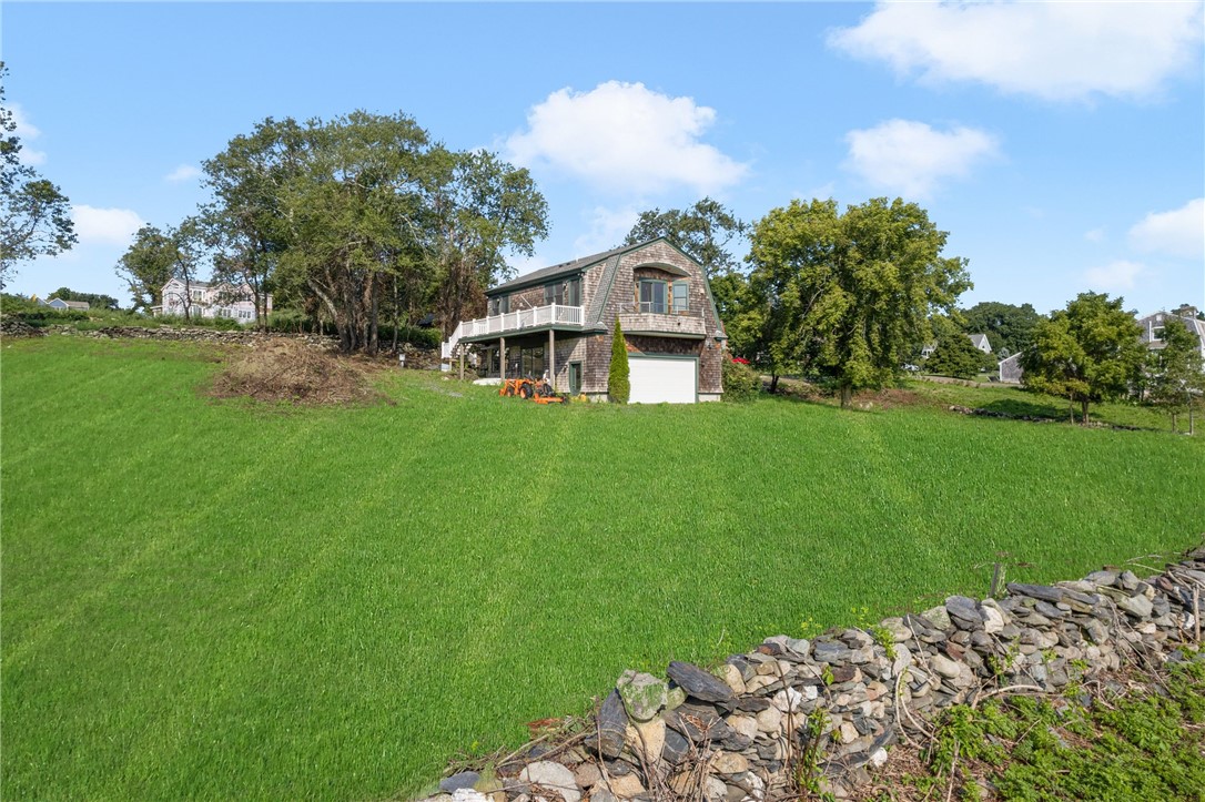Shingle-sided home with an elevated deck and garage above a broad lawn and stone wall.