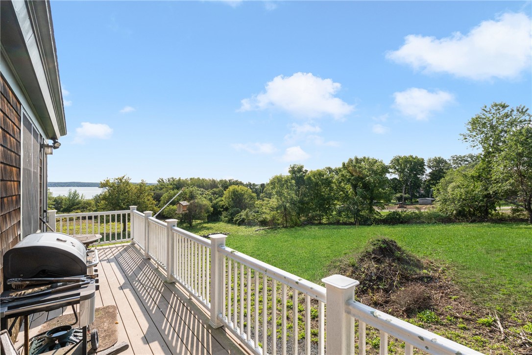 Deck overlooking a green lawn and distant water, with white railings and a barbecue.