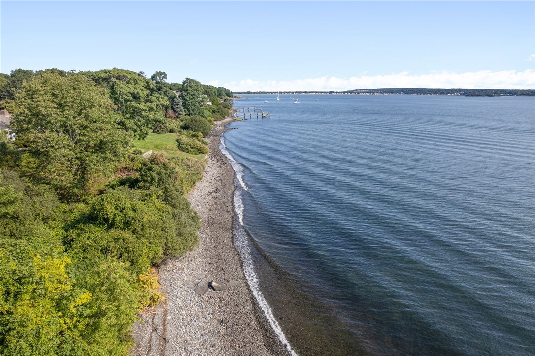 Aerial view of a wooded shoreline curving beside open water, with a dock and sailboats offshore.