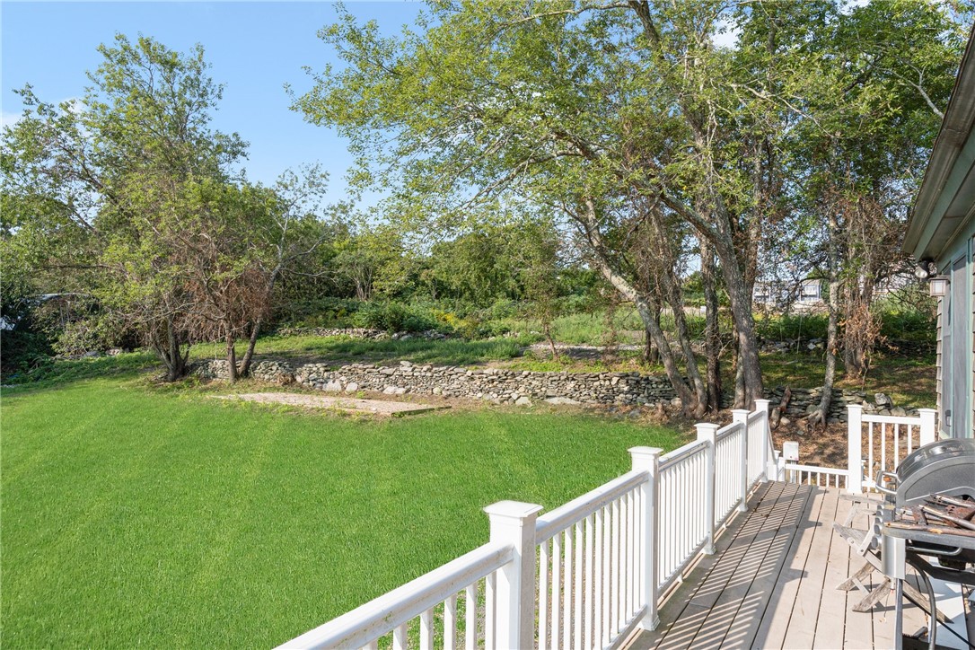 Backyard with a broad lawn, mature trees, stone wall, and deck with white railings.