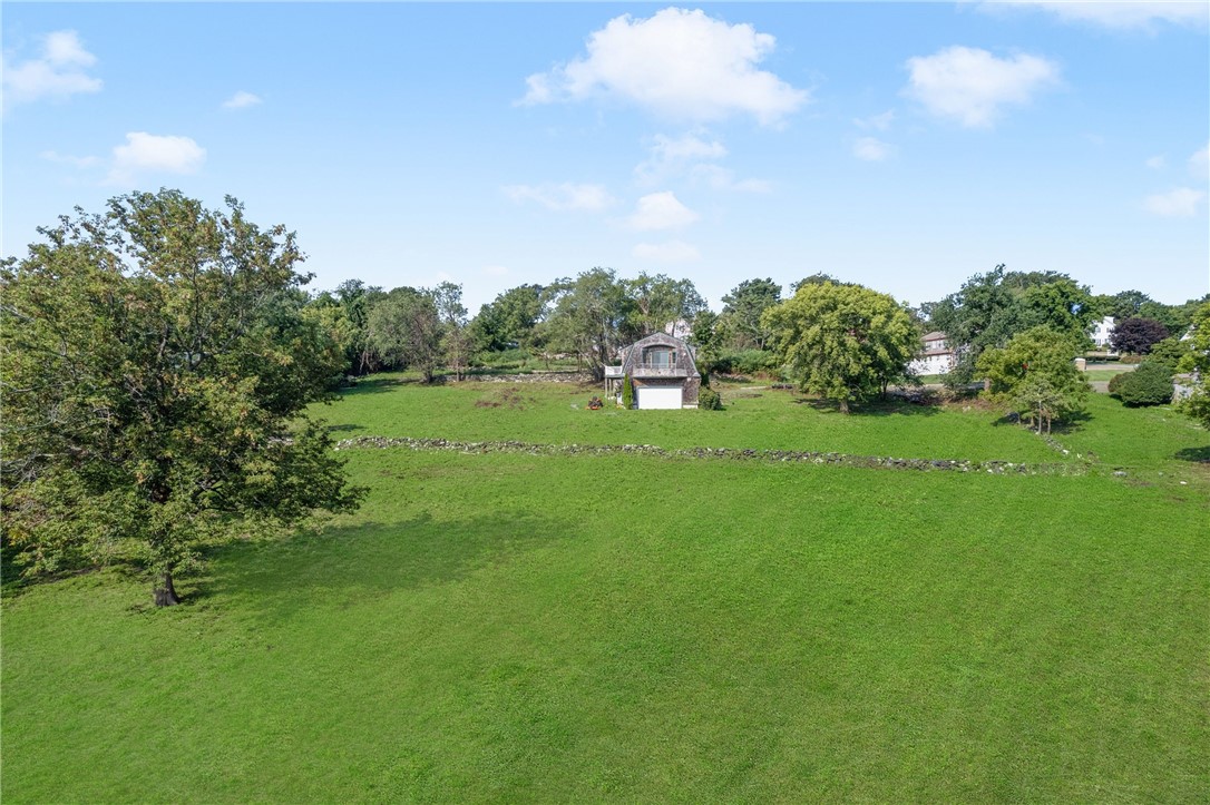 Aerial view of a broad green property with a small outbuilding, mature trees, and a stone wall.