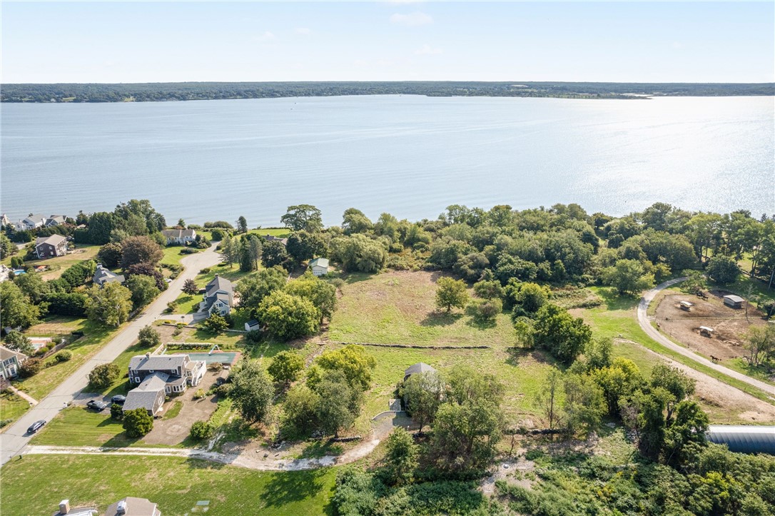 Aerial view of a wooded waterfront property with an open lot beside a broad bay.