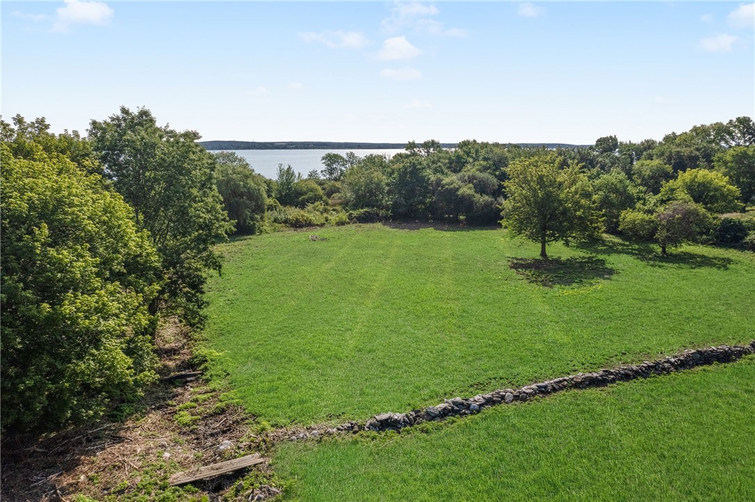 Grassy property bordered by trees and a stone wall, with water visible beyond.
