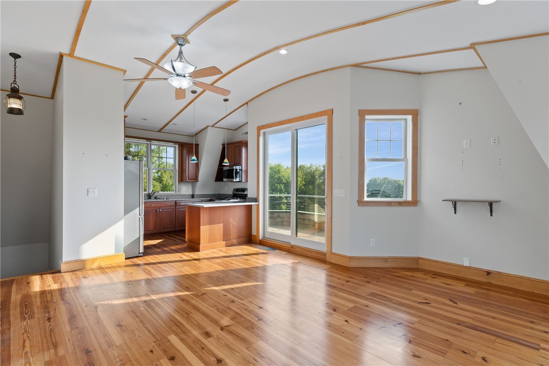 Open living room and kitchen with hardwood floors, exposed ceiling beams, and sliding glass doors to a deck.