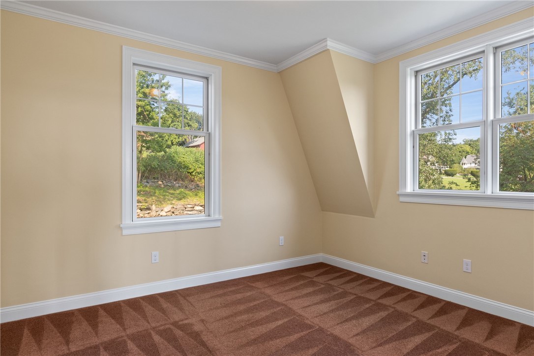 Empty bedroom with brown patterned carpet, beige walls, and windows overlooking trees and a lawn.
