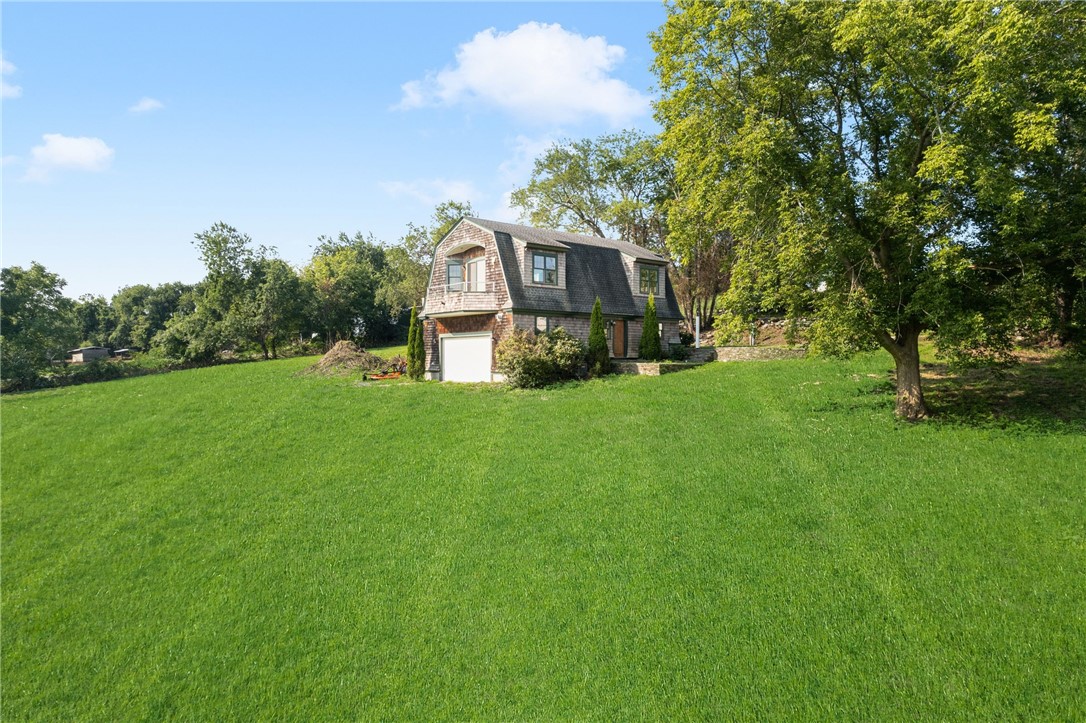 Shingled house with garage set behind a broad lawn and mature trees.