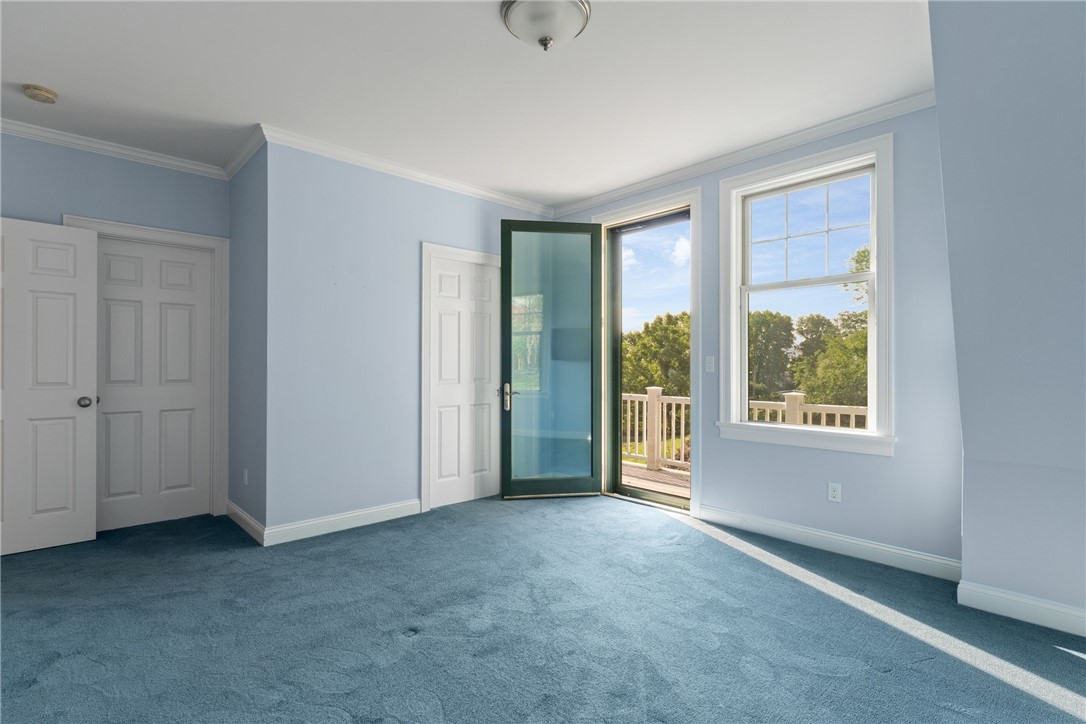 Empty blue-carpeted room with pale blue walls, a large window, and an open door to a balcony.