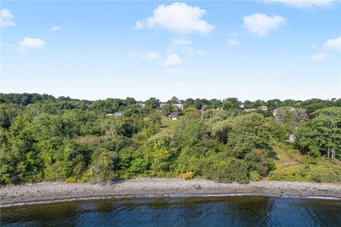 Aerial view of wooded waterfront with a rocky shoreline and homes among the trees.