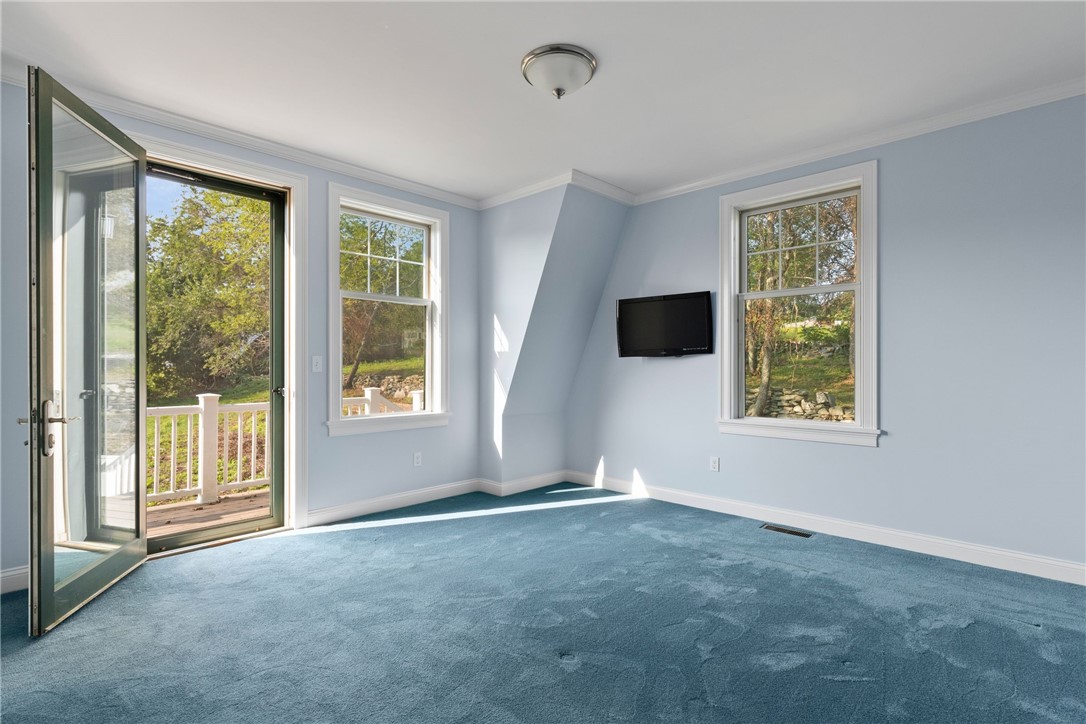 Empty blue-carpeted room with a wall-mounted television and an open door to the deck.