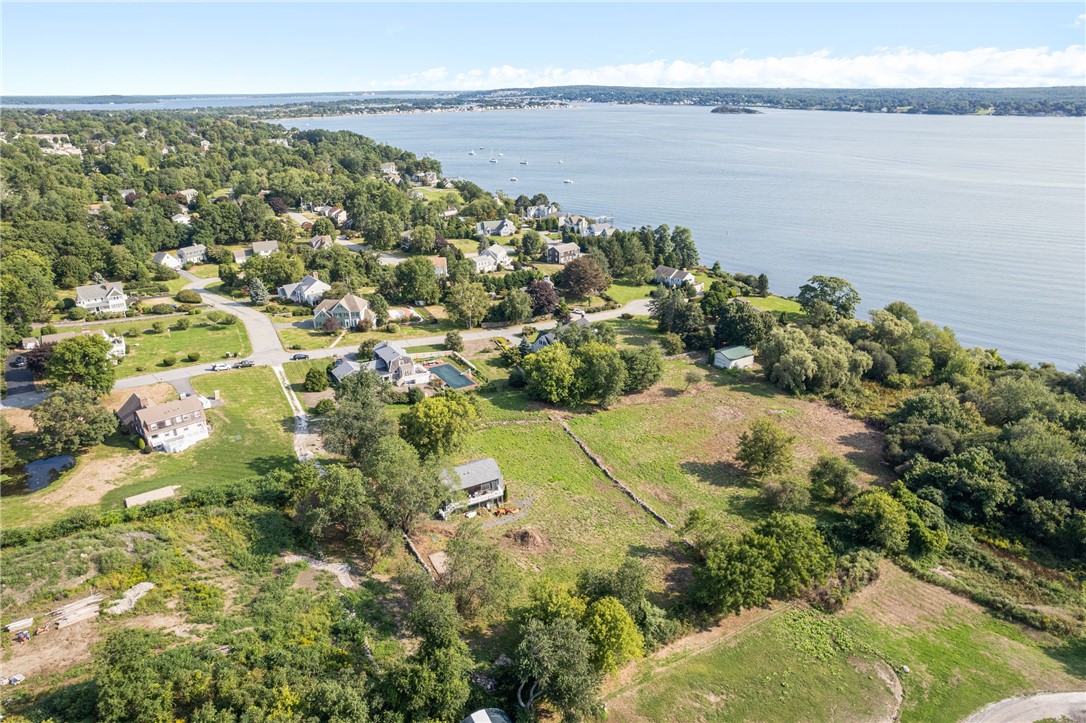 Aerial view of an open, partly wooded parcel beside a coastal neighborhood and bay.