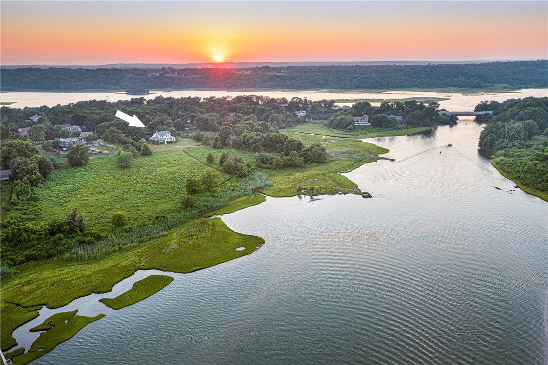Aerial sunset view of a white house beside marshland and winding coastal water.