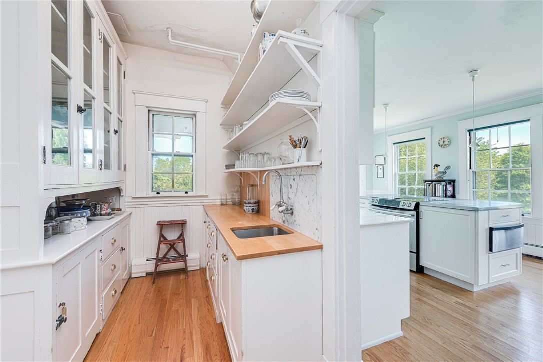 Bright white kitchen with butcher-block counters and open shelving, opening to a larger kitchen with an island.