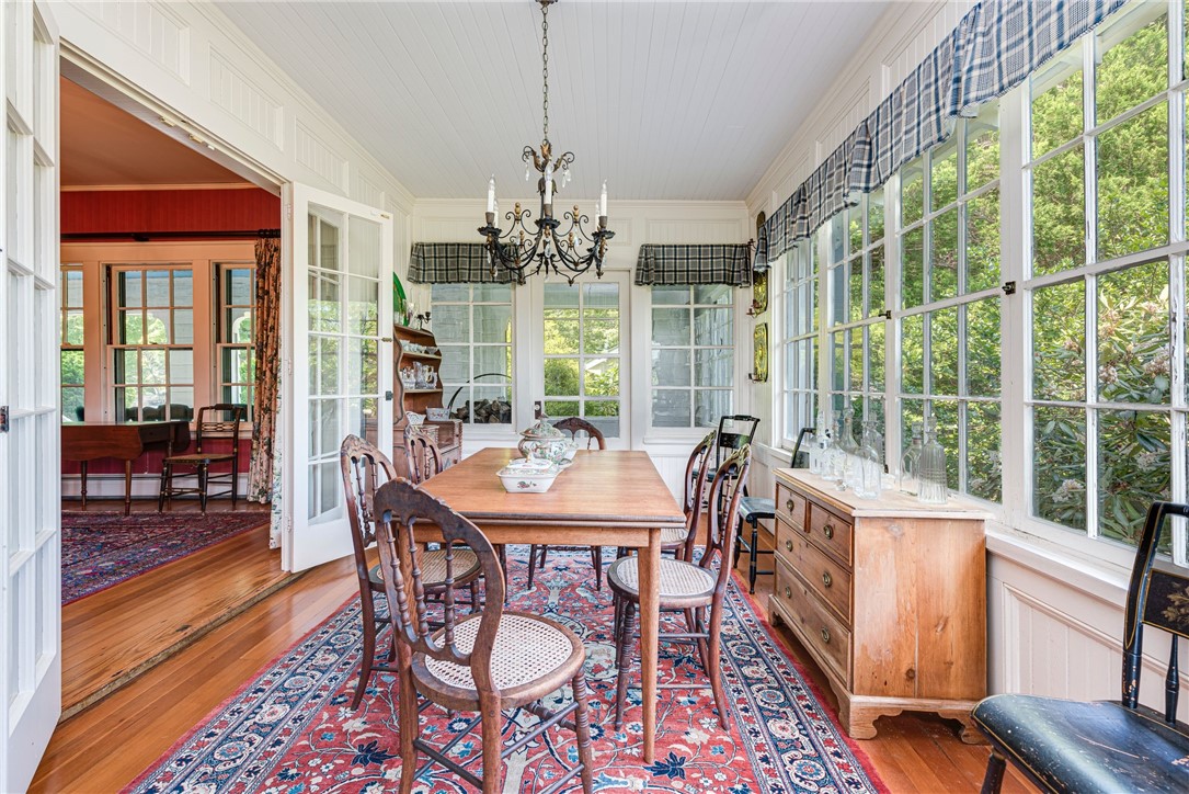 Dining room with tall windows, a wooden table, patterned rug, and chandelier.