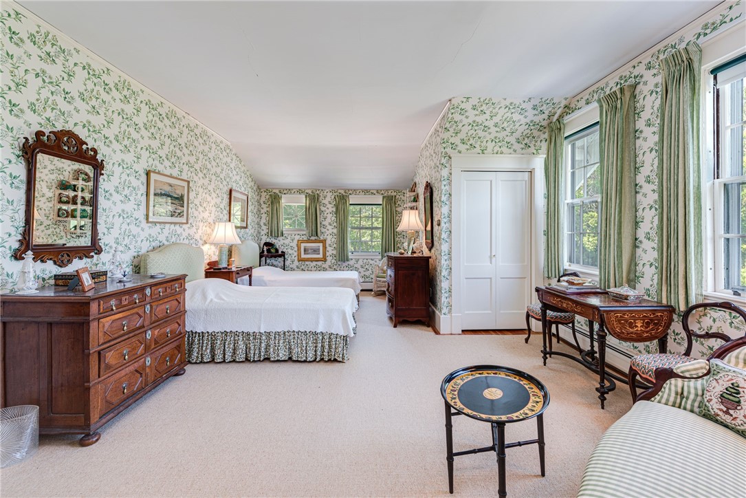 Bedroom with two white-covered beds, green floral wallpaper, and antique wooden furniture.