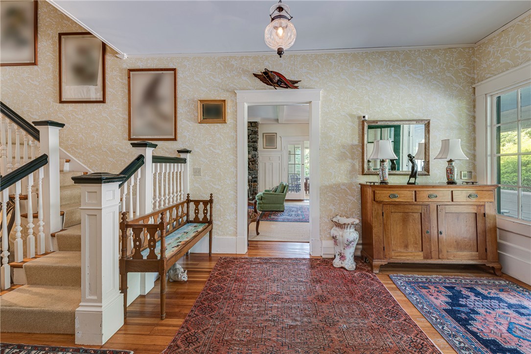 Entry hall with a carpeted staircase, patterned wallpaper, antique rugs, and a wooden sideboard.